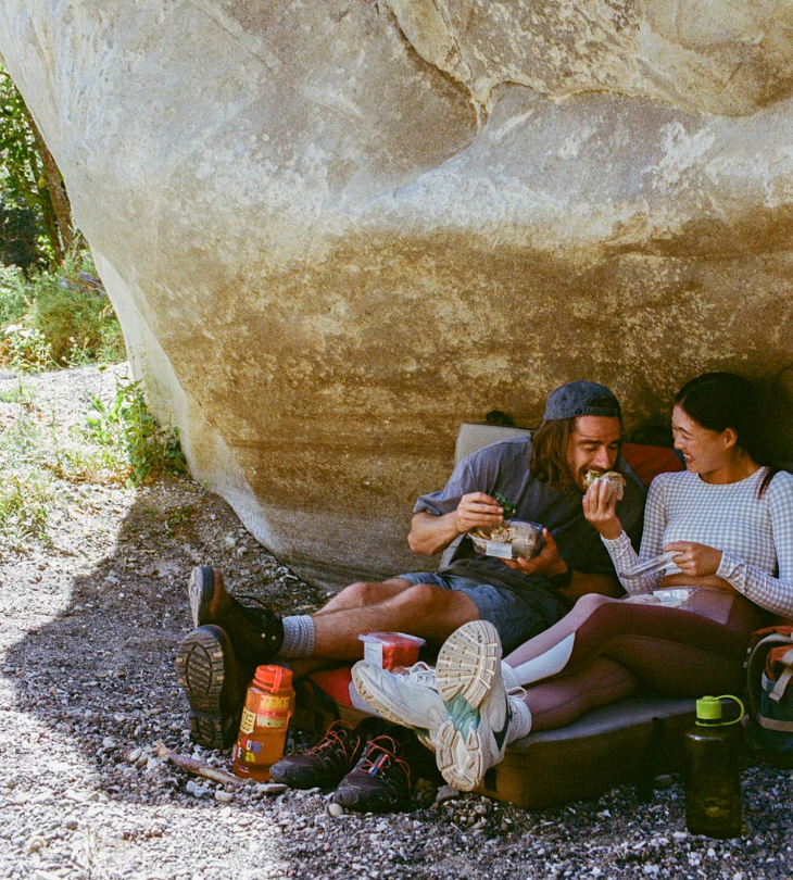 two people eating some food and laughing in the outdoors