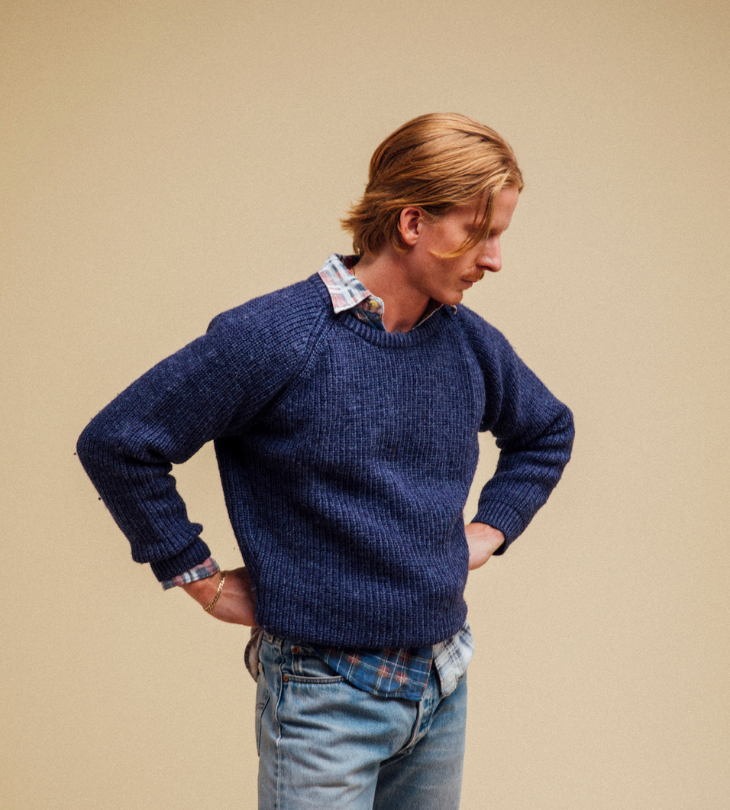 a man in a navy sweater over plaid shirt standing in front of a yellow background