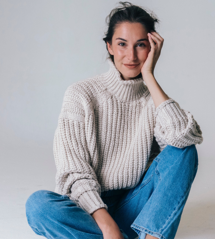 a woman sitting on the ground wearing a chunky sweater and jeans