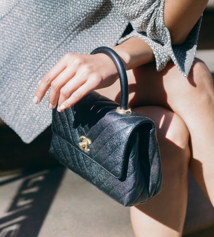 a woman sitting on a stoop in grey jacket and black Chanel bag on her wrist